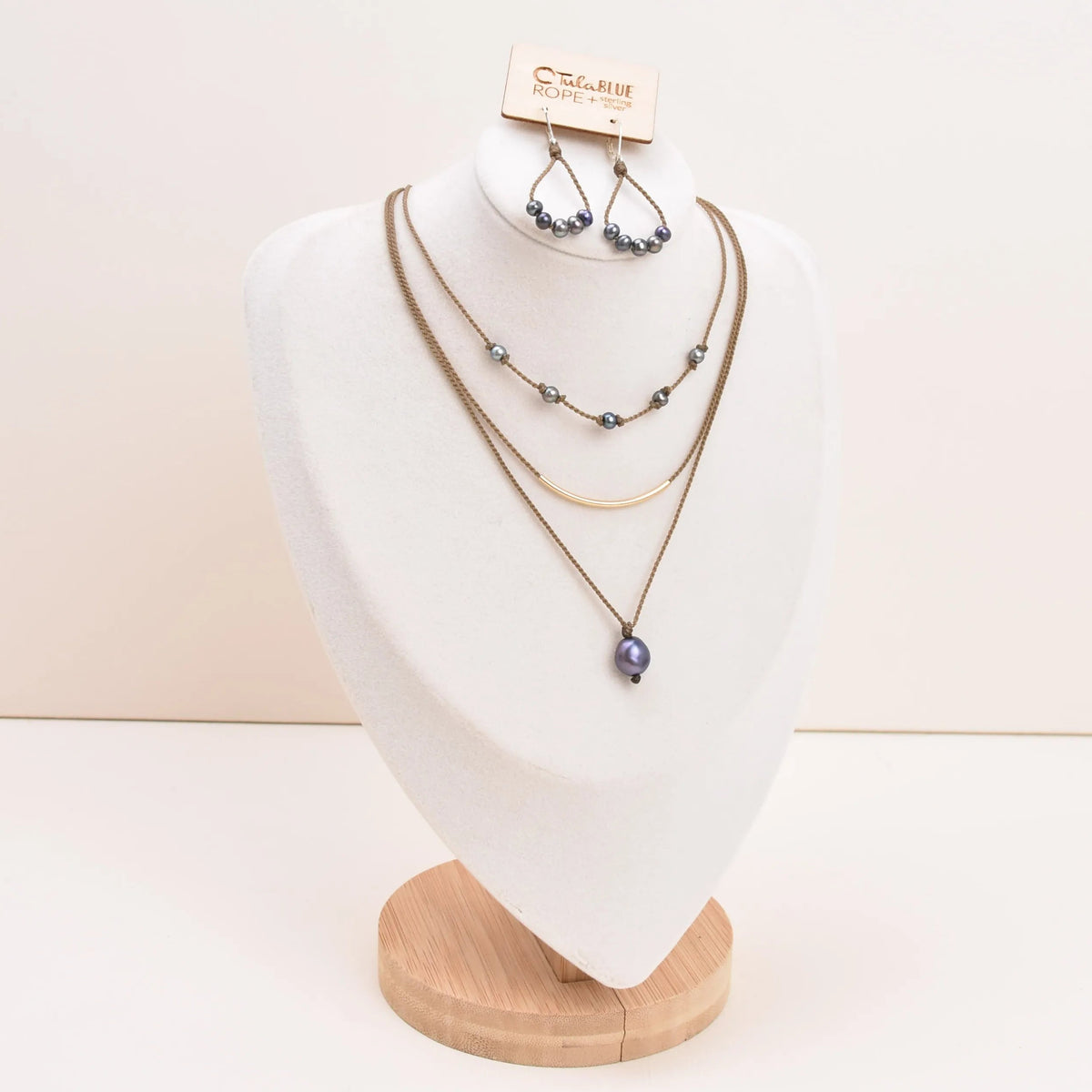 Dripping in Pearls necklace stack with earrings in peacock on bust with white background