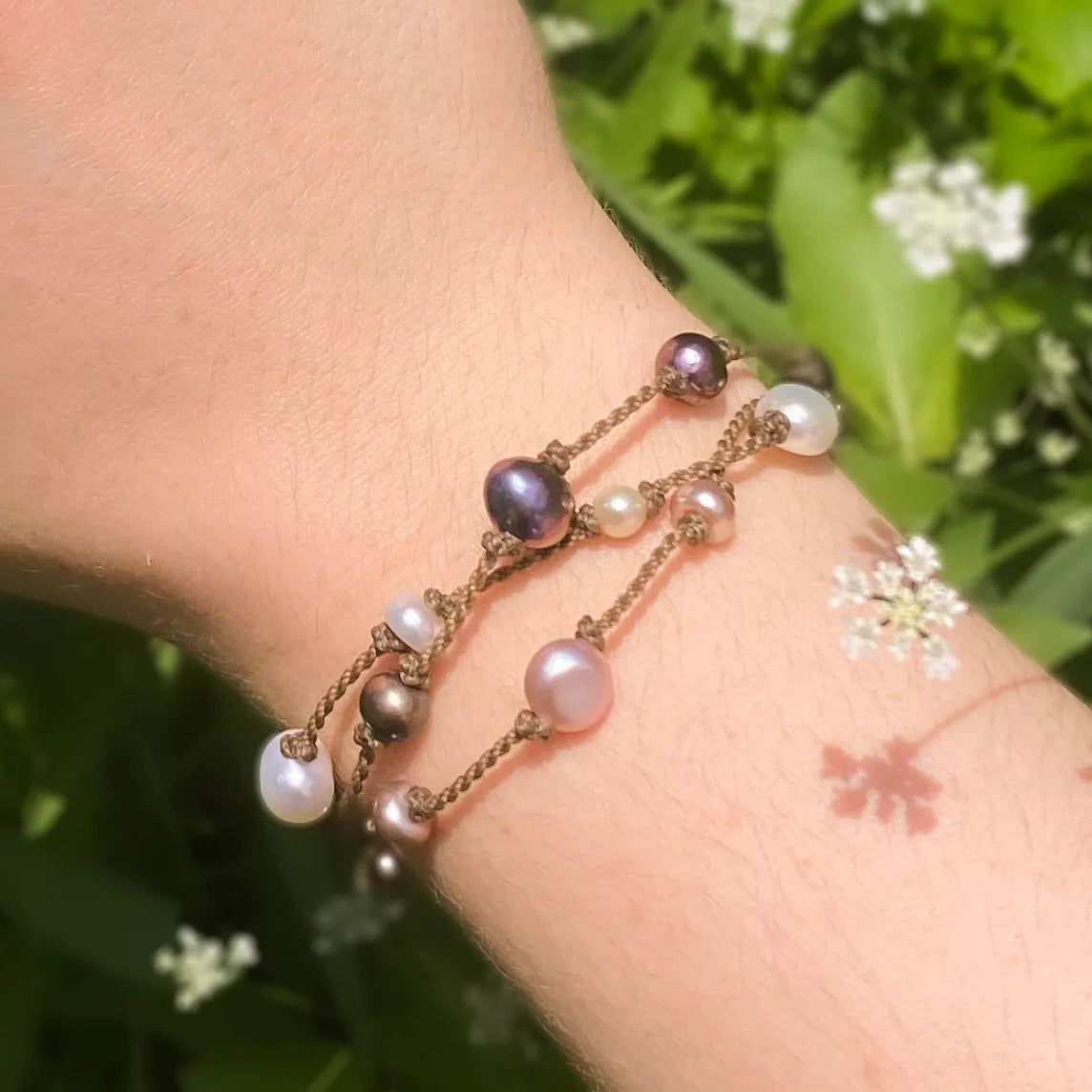 Tula Blue's Journey Bracelet in mixed pearl on model wrist in front of greenery closeup