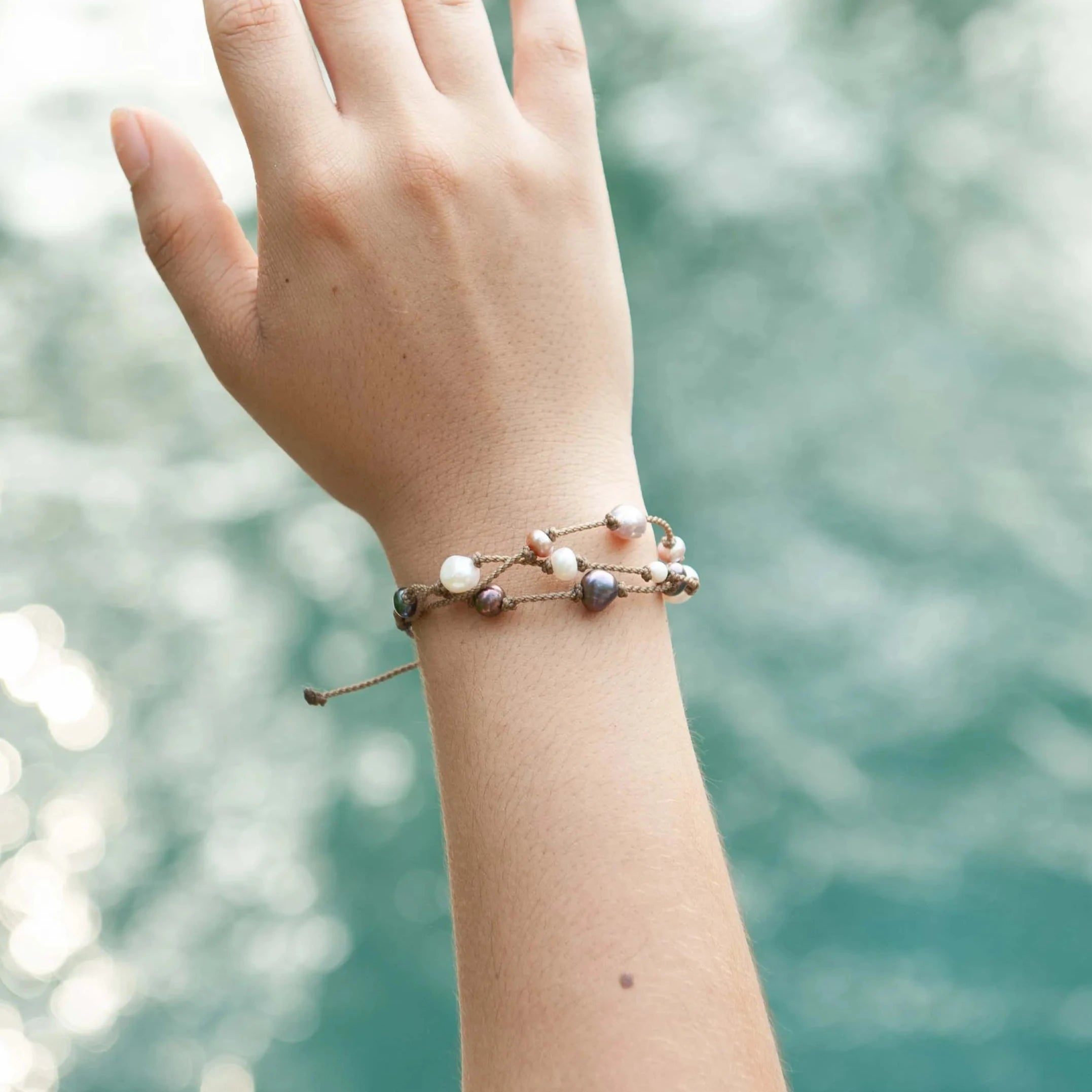 Tula Blue's Journey Bracelet in mixed pearl on model wrist and hand in front of water