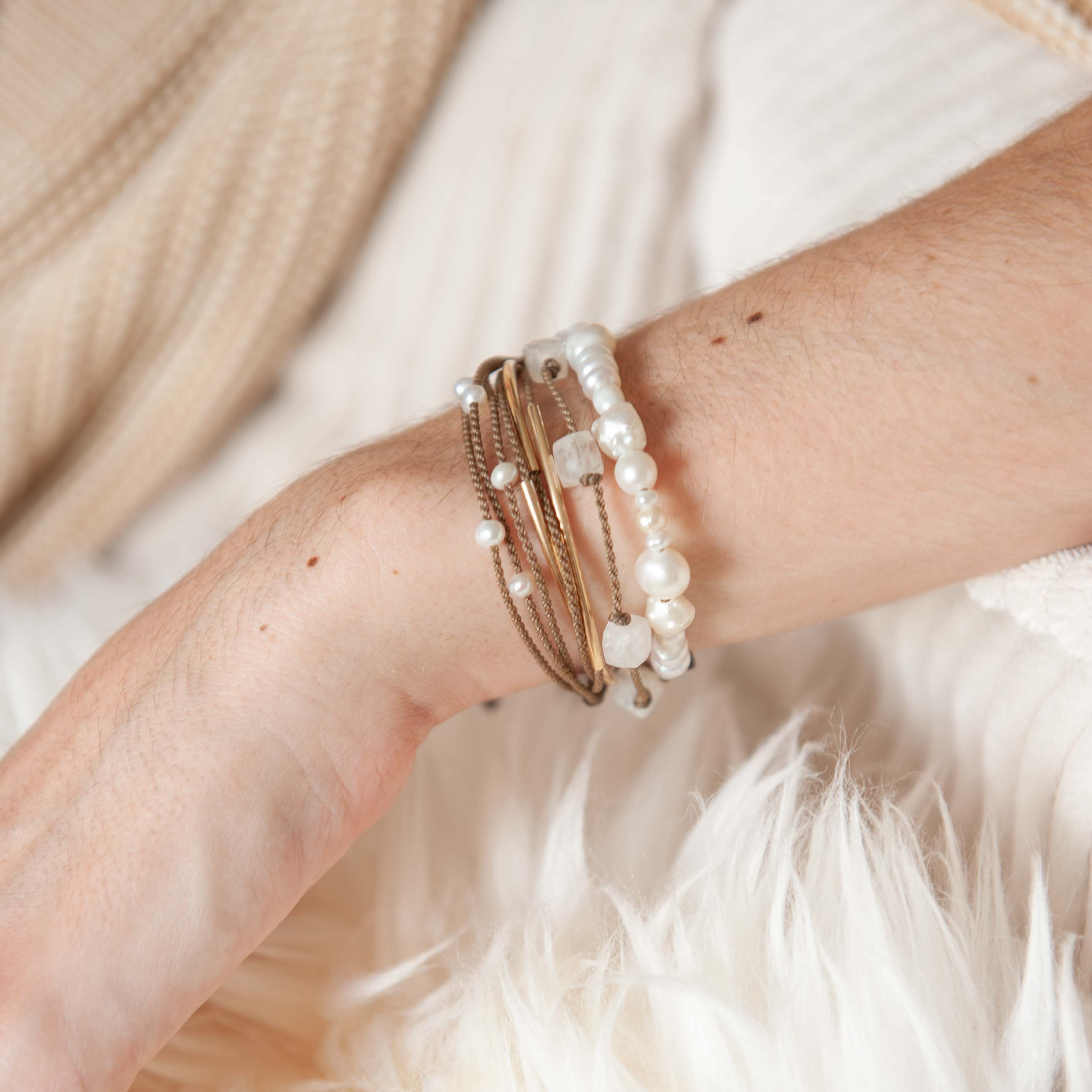 Close-up of a wrist wearing multiple pearl Tula Blue bracelets on a soft, light-colored surface.