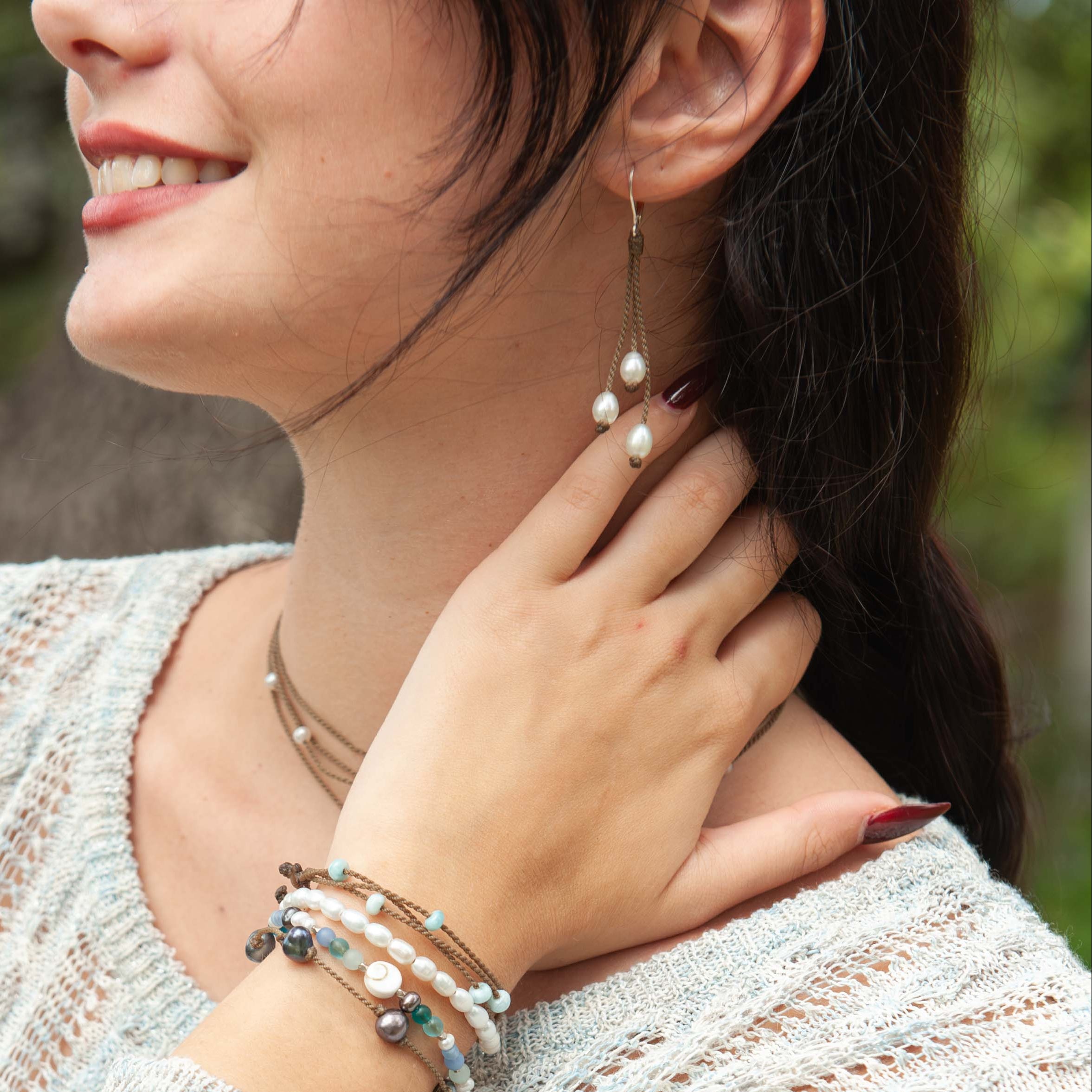 Woman wearing a light sweater with Tula Blue bracelets, earrings and a necklace, outdoors.