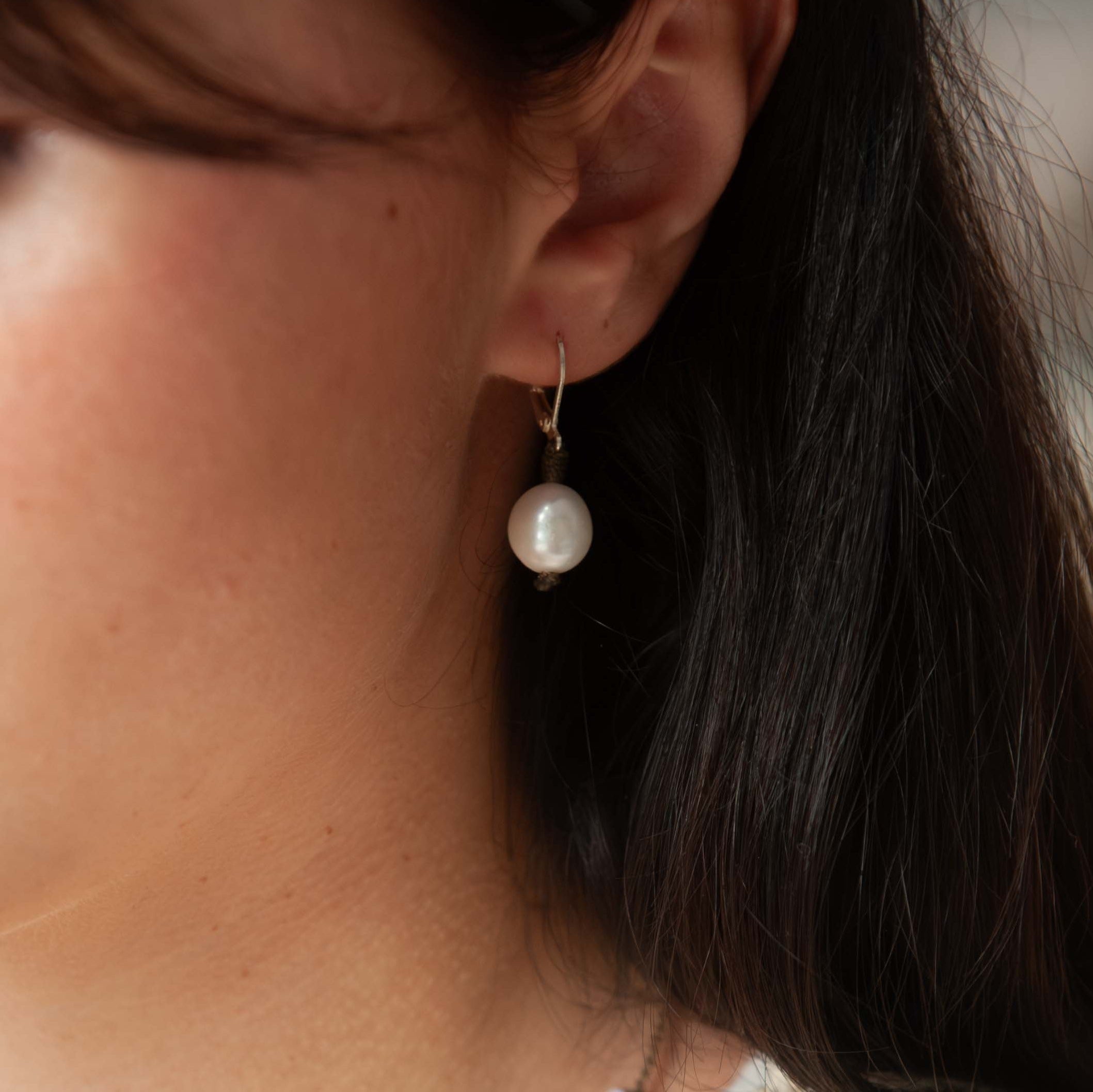 Close-up of a person wearing pearl earrings with a blurred background