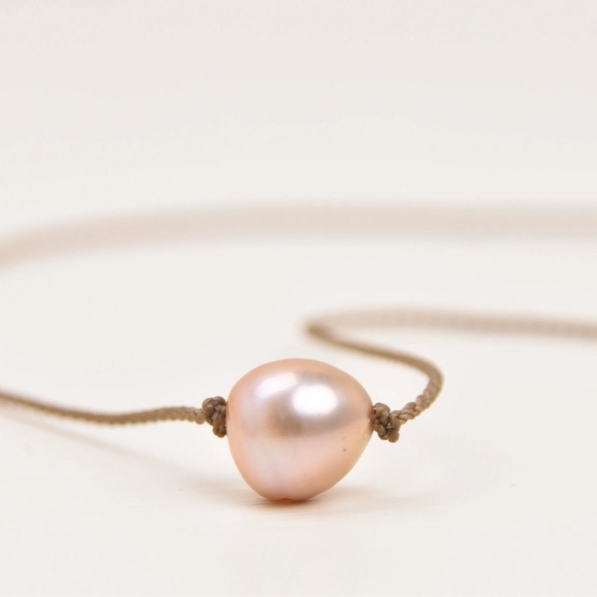 Close-up of a blush pink Edison freshwater pearl knotted on the Classic Pearl Necklace's hand-spun waterproof rope