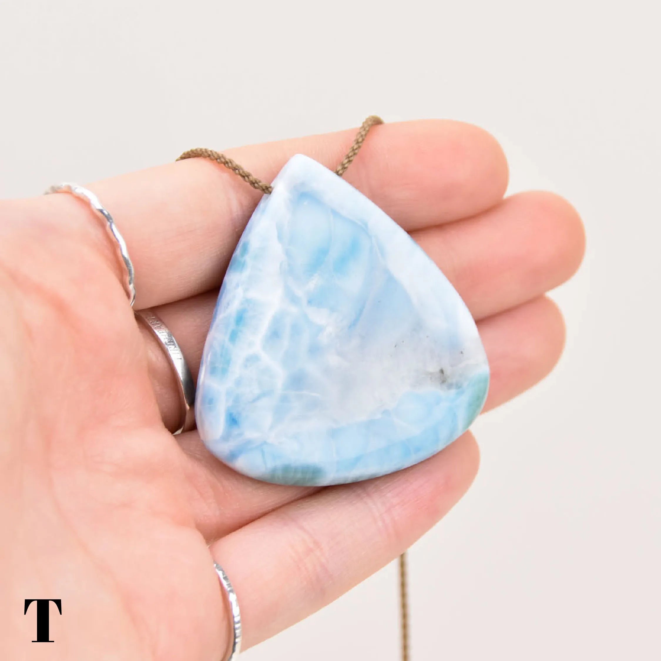 Triangular larimar pendant held in a hand against a neutral background
