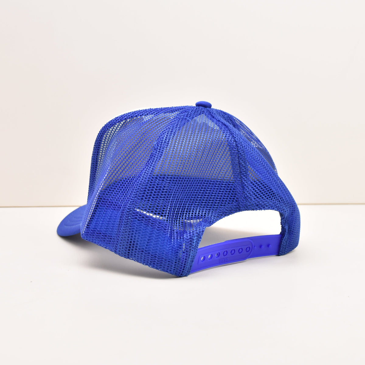 A bright blue trucker-style cap with a mesh back and adjustable strap, photographed from the side on a plain white background.