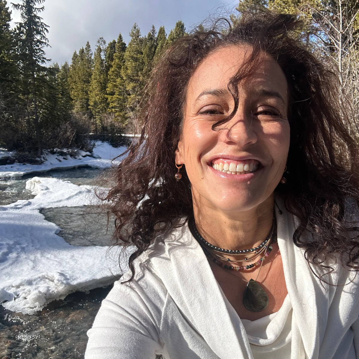 heather macrae stringer smiling outdoors with trees and water in the background, wearing her watermelon tourmaline adjustable necklace