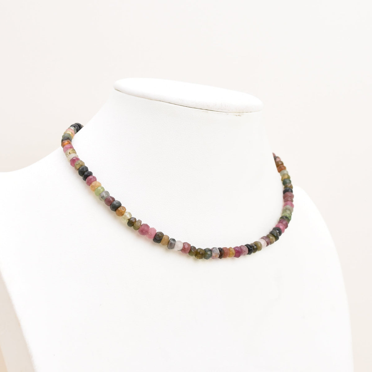 A watermelon tourmaline necklace displayed on a white mannequin bust against a plain off-white background.