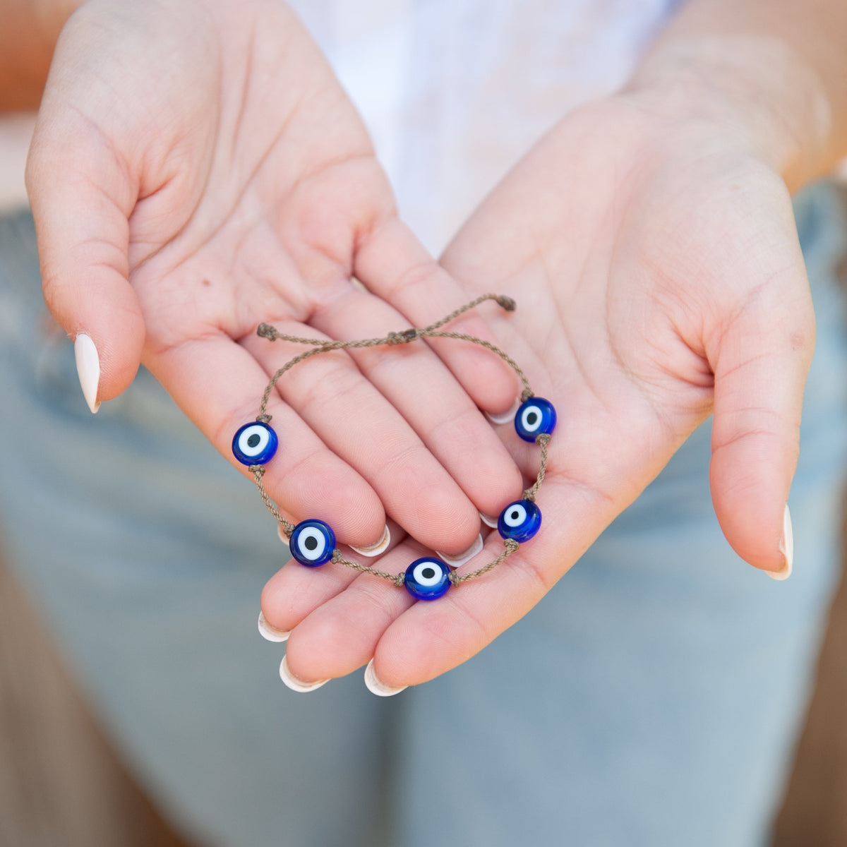 Evil Eye Bracelet resting in open hands, blue glass evil eye beads on waterproof rope