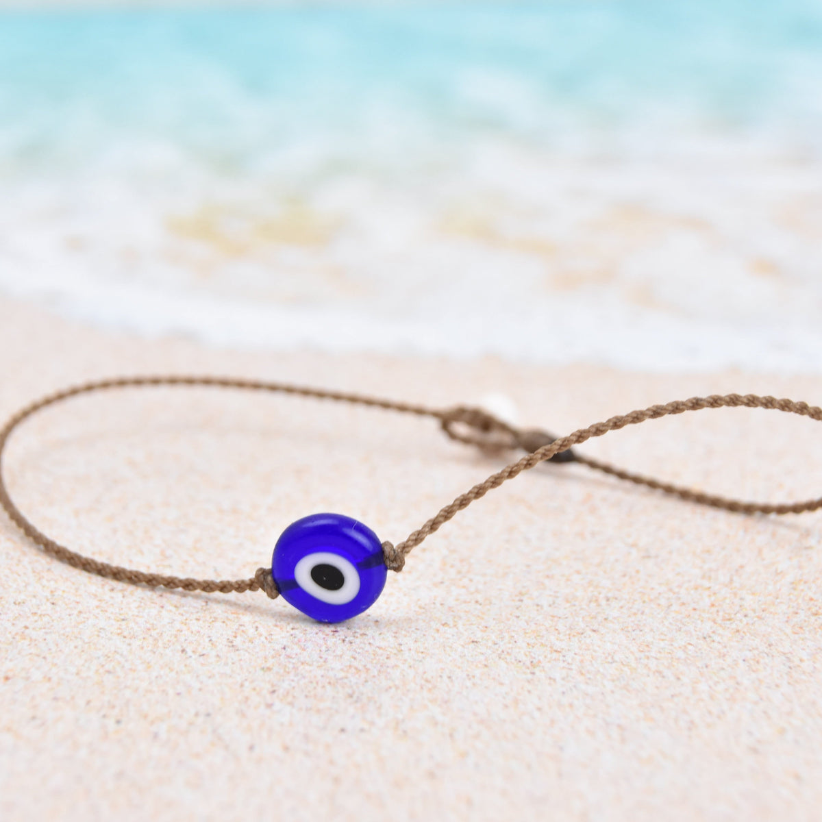 Evil Eye Anklet, Classic style close-up of one blue glass evil eye bead on hand-spun rope on beach sand