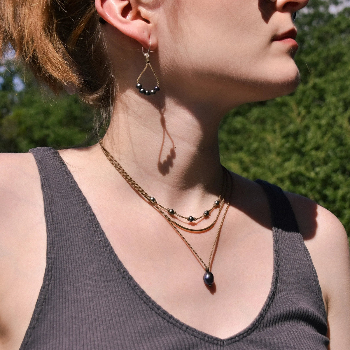 Dripping in Pearls necklace stack with earrings in peacock on model with trees in background