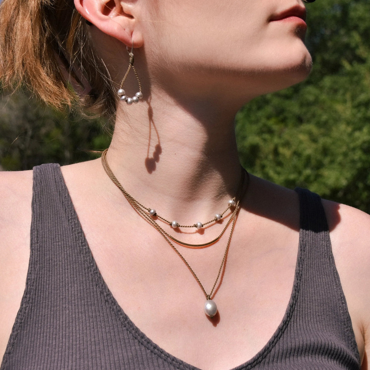 Dripping in Pearls necklace stack with earrings in silver on model with trees in background