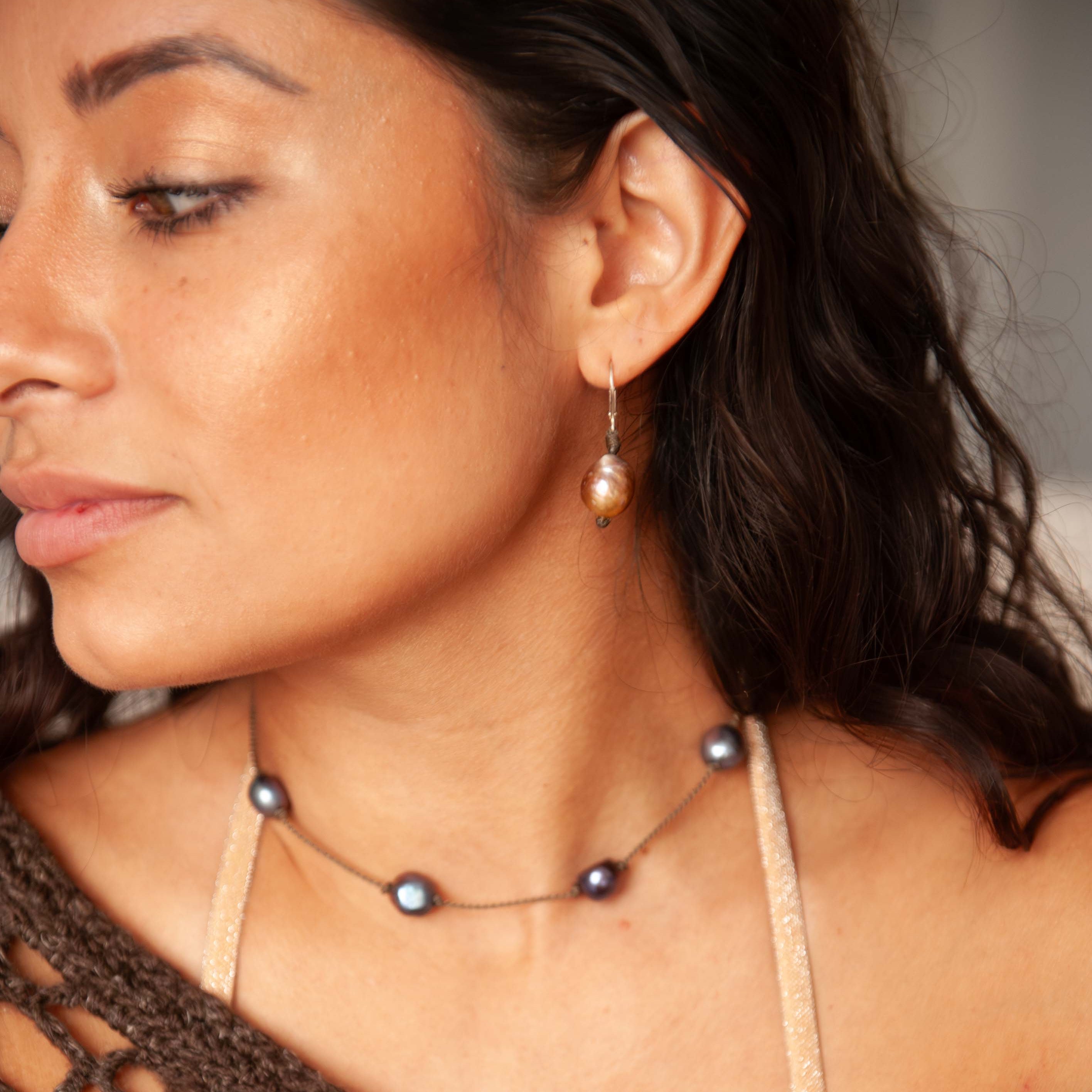Woman wearing a brown crochet top and Tula Blue pearl earrings with a blurred background