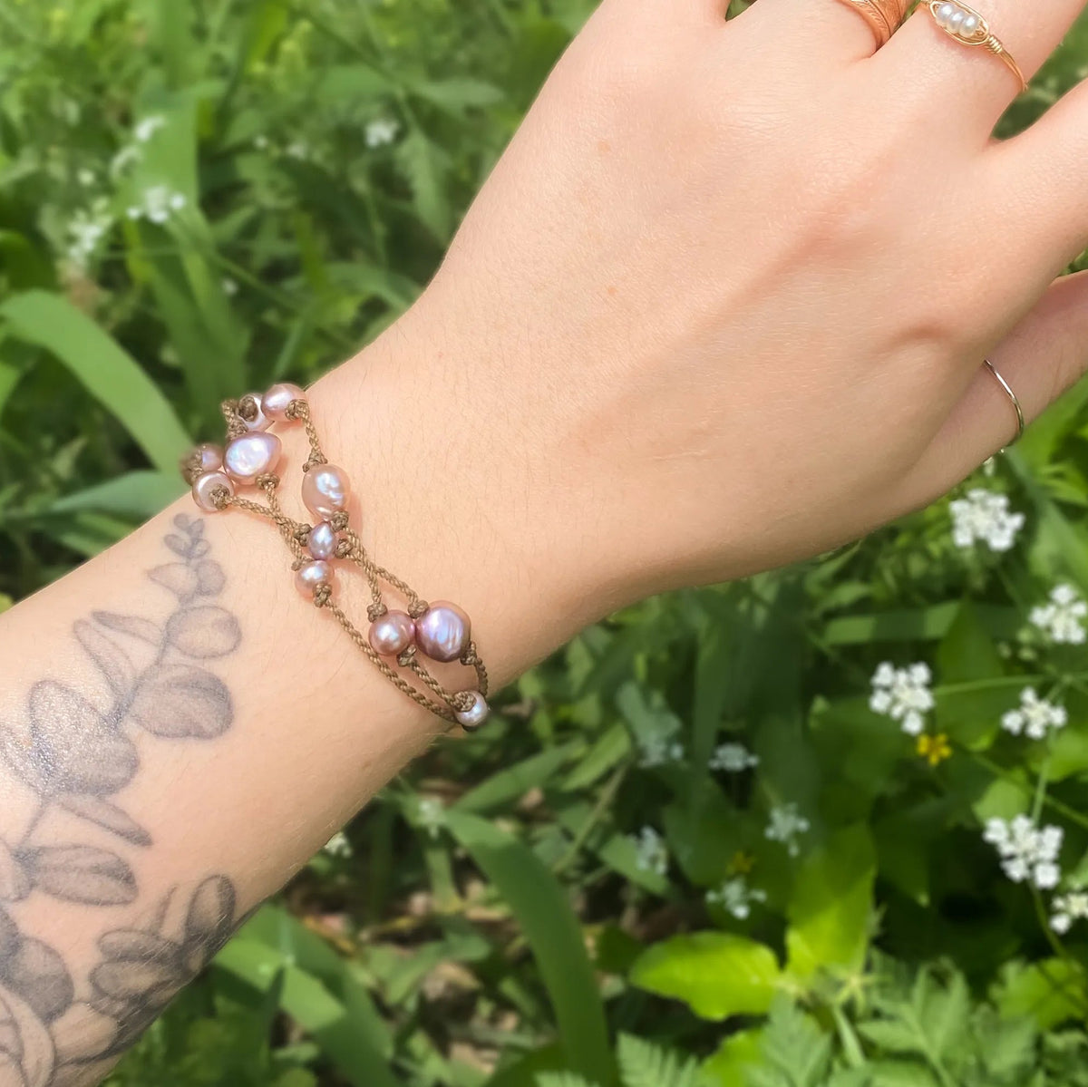 Tula Blue's Journey Bracelet in blush pearl on model wrist in front of greenery