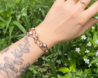 Tula Blue's Journey Bracelet in blush pearl on model wrist in front of greenery