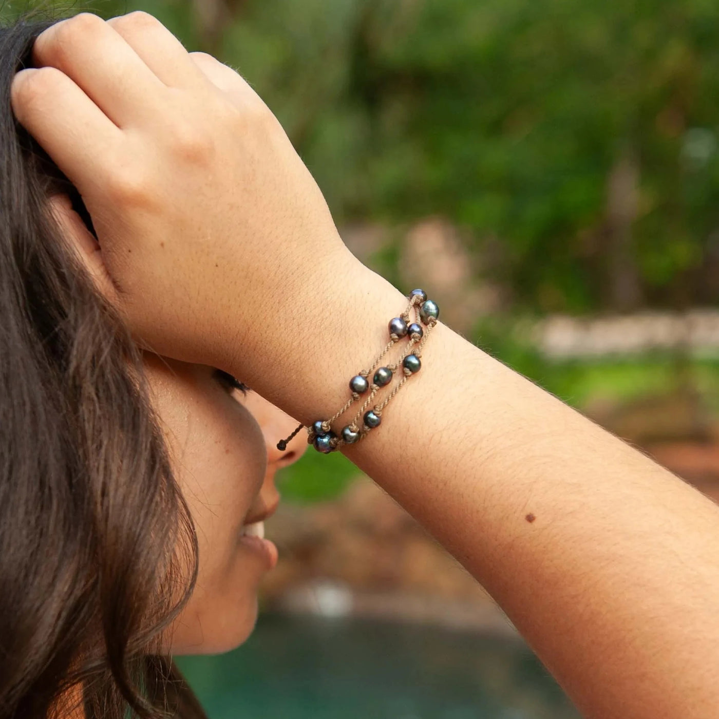 Tula Blue's Journey Bracelet in peacock pearl on model wrist, hand on head in front of pool with greenery 