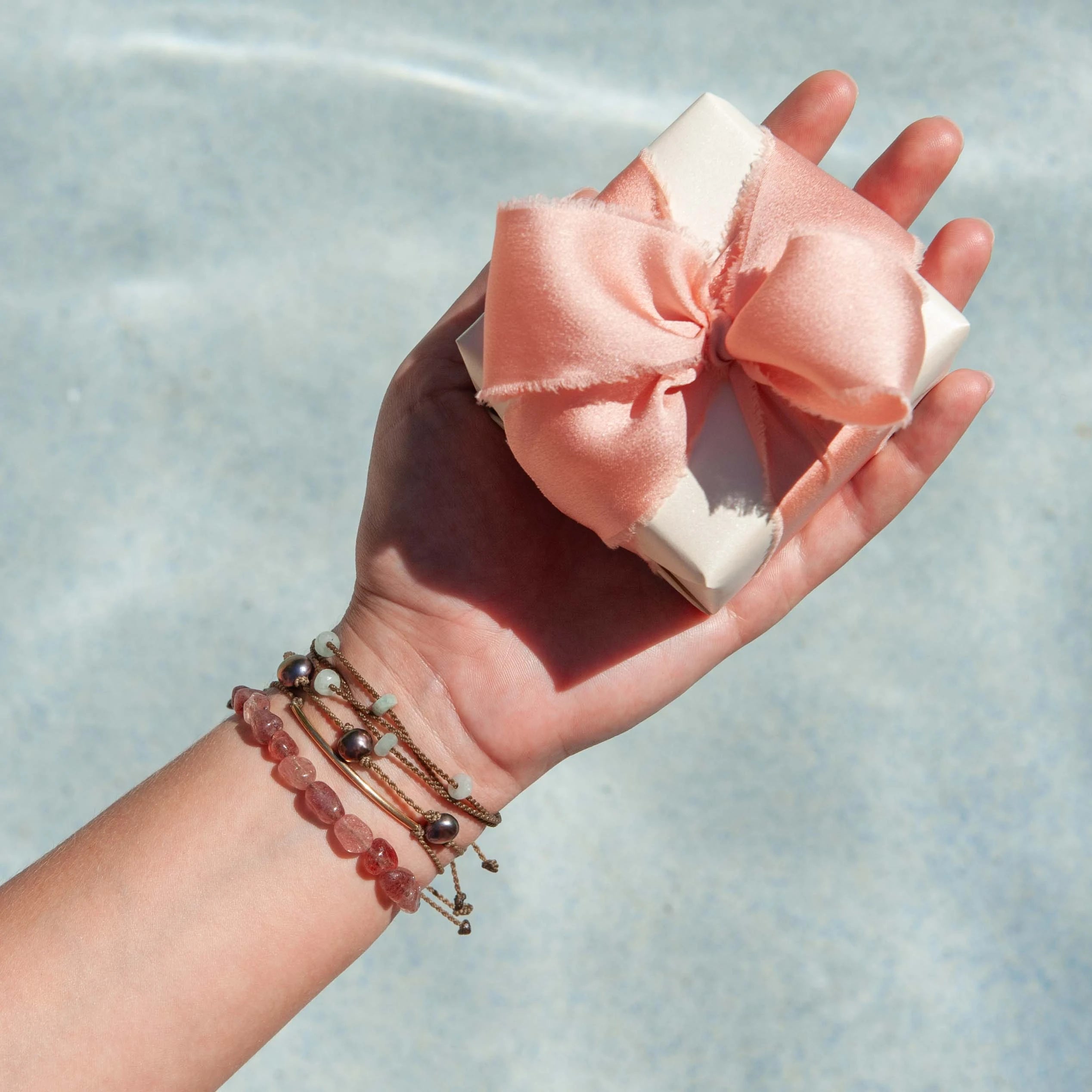 Hand holding a gift box with a pink bow with a blurred water background