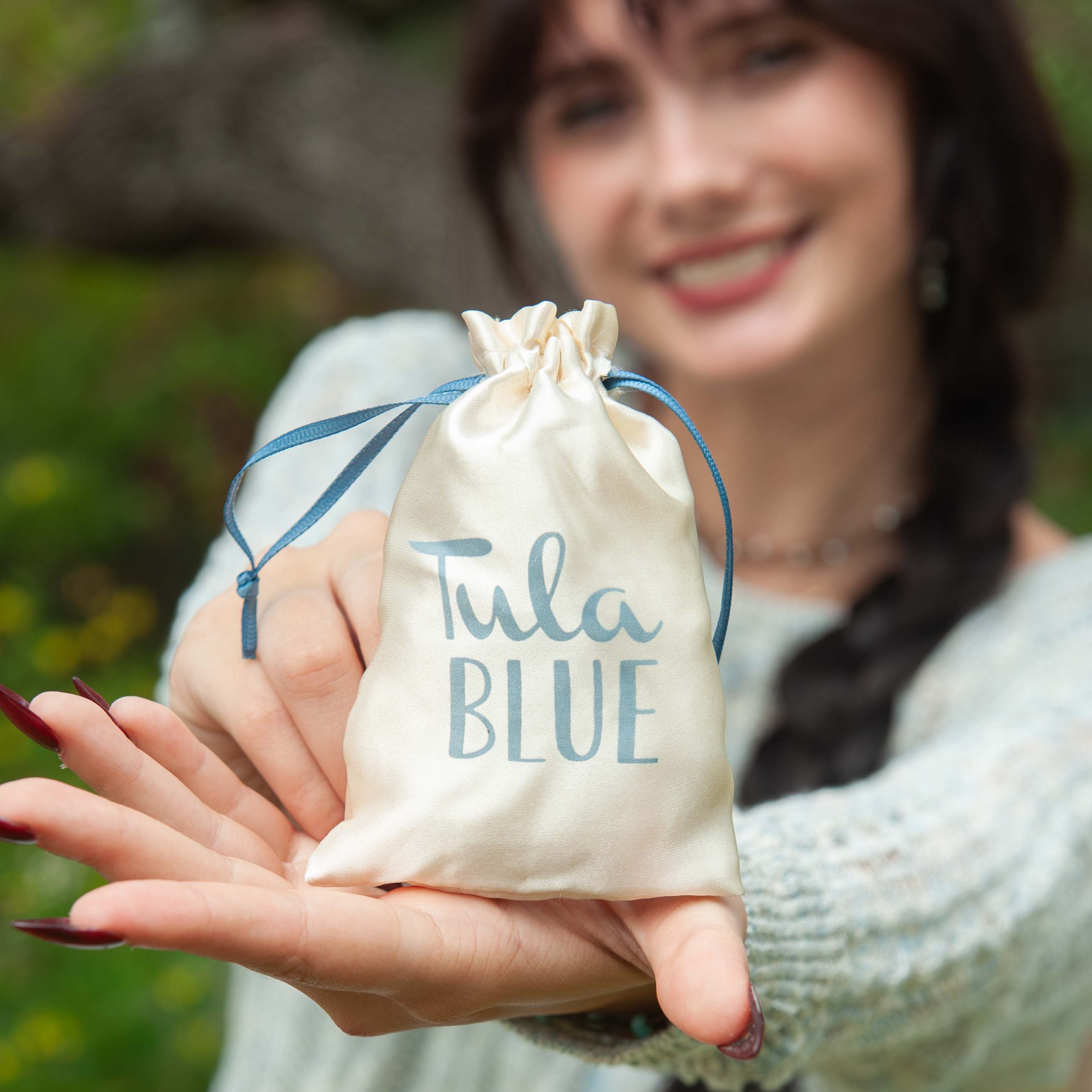 Woman holding a 'Tula Blue' product in a drawstring bag outdoors.