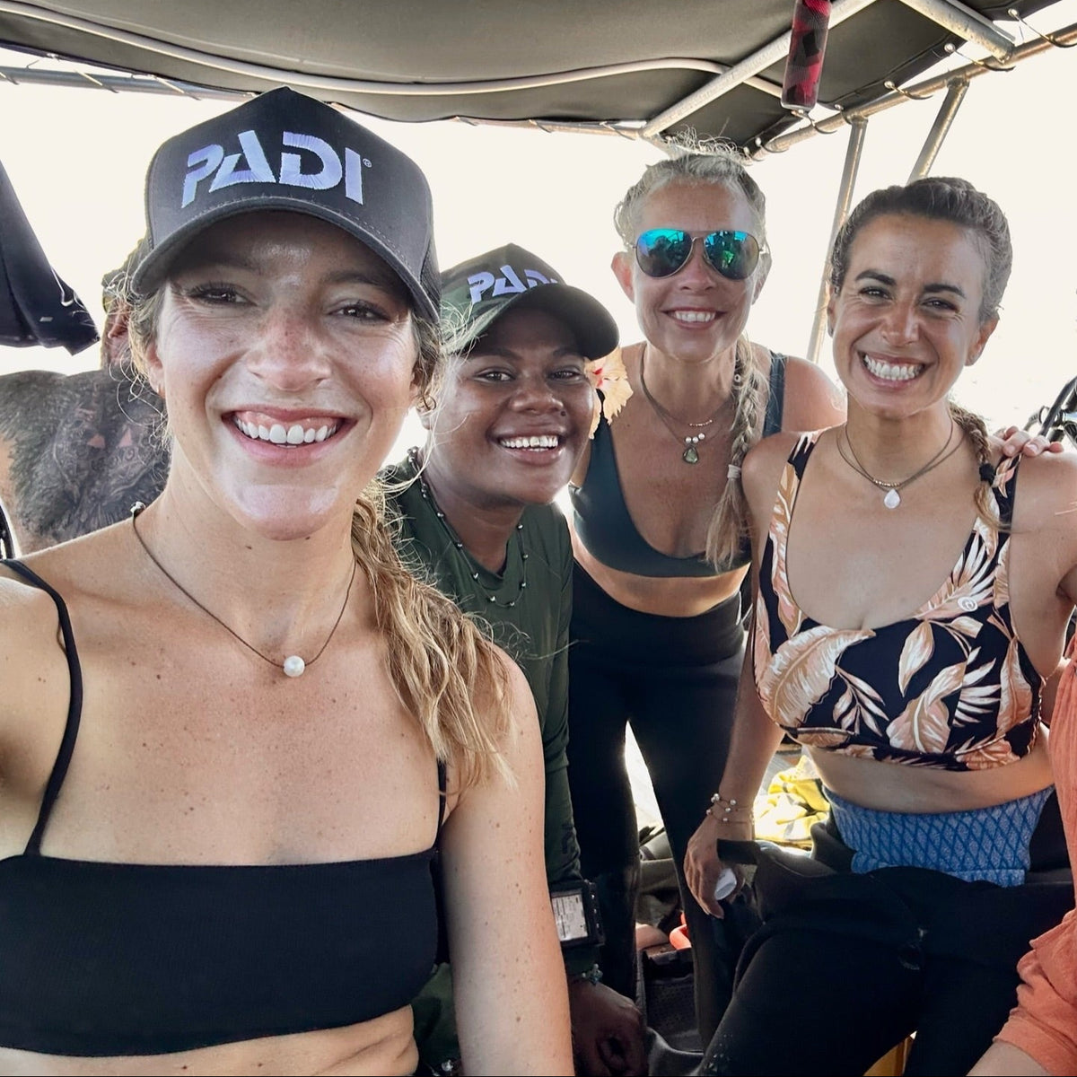 Four women smiling on a dive boat in Fiji, two in PADI hats, one wearing the Classic Pearl Necklace with a white freshwater pearl on hand-spun rope