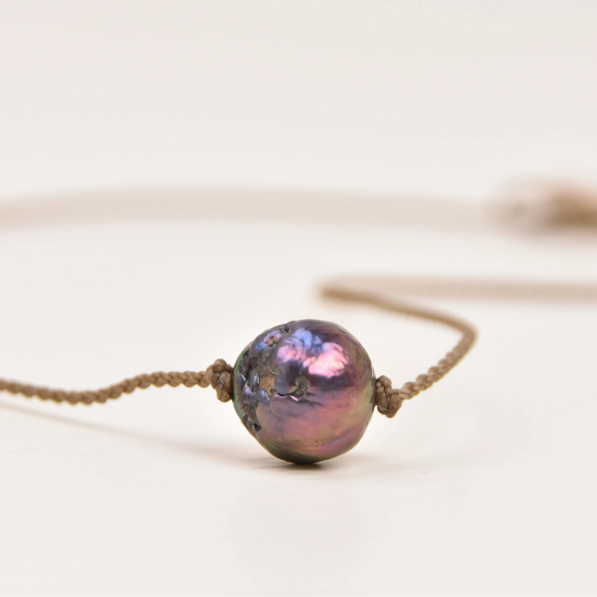 Close-up of a peacock Edison freshwater pearl with pink and purple shine, knotted on hand-spun waterproof rope