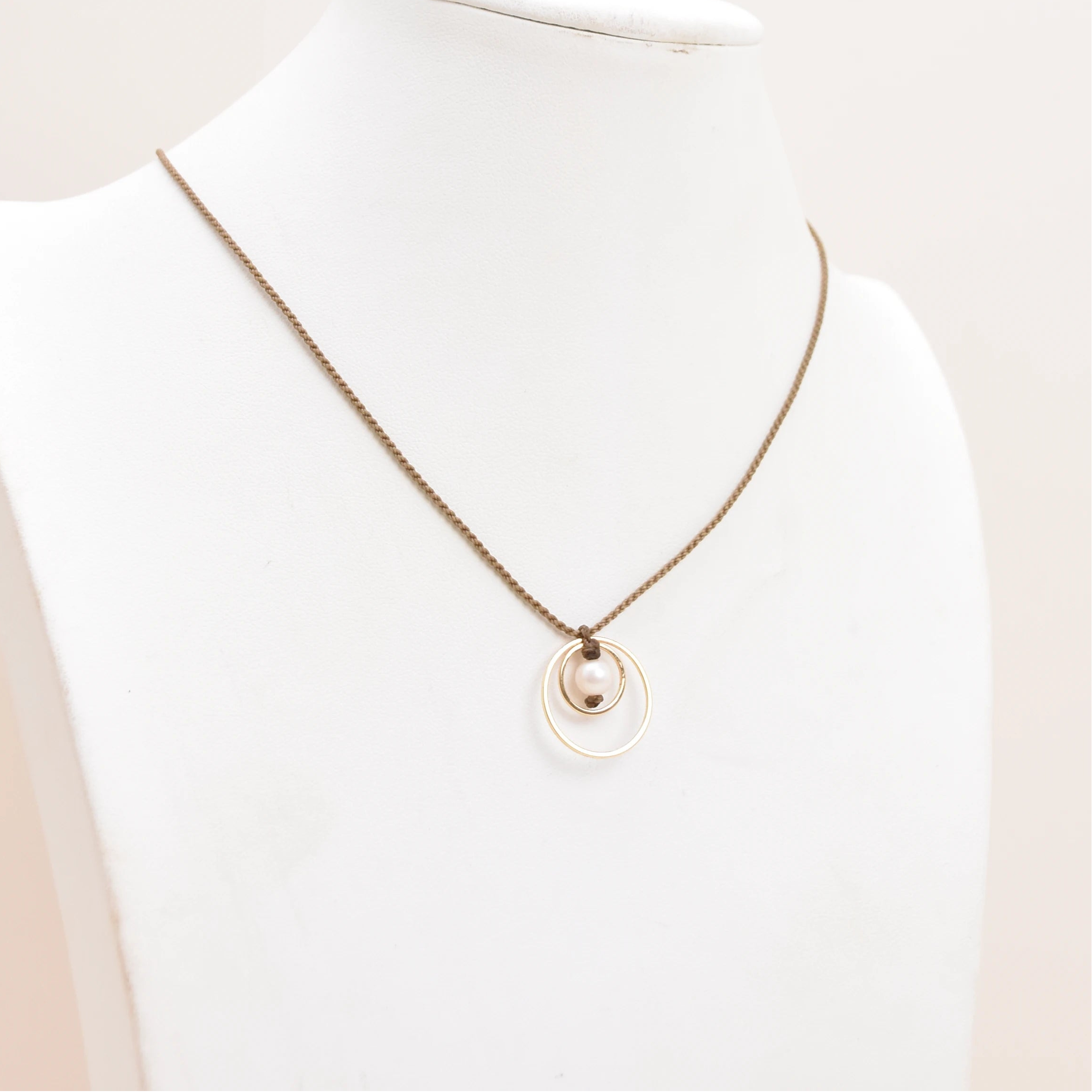 A delicate rope chain necklace with a minimalist pendant displayed on a white mannequin bust against a soft, light beige background.