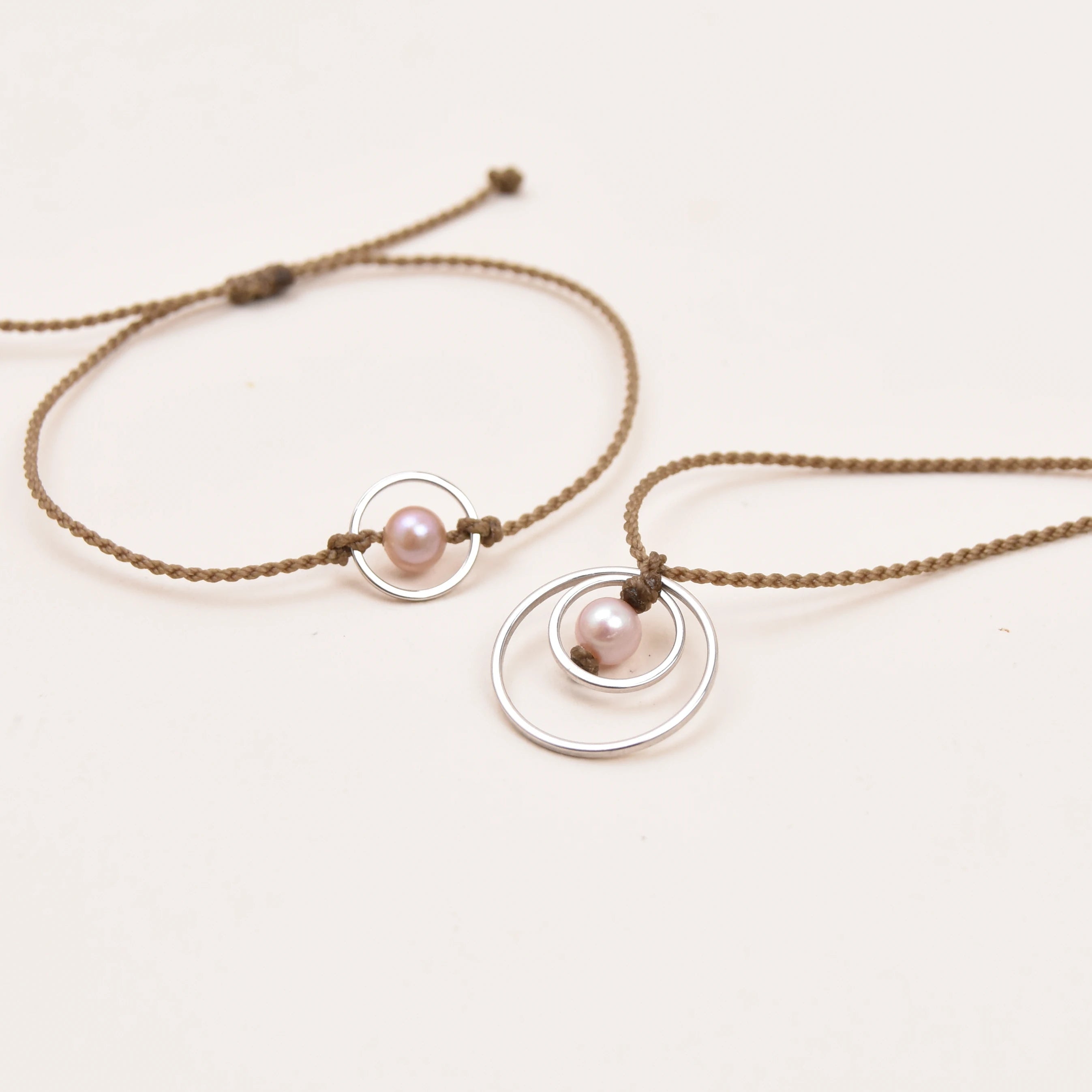A matching jewelry set featuring a rope bracelet and necklace, each adorned with a small pink pearl and a silver circle, displayed on a clean white background.