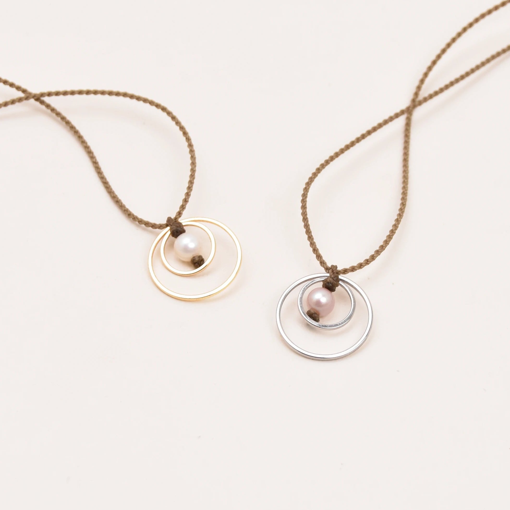 Two minimalist pendant rope necklaces with circular disc pendants, one in gold and one in silver, displayed on a clean white background.