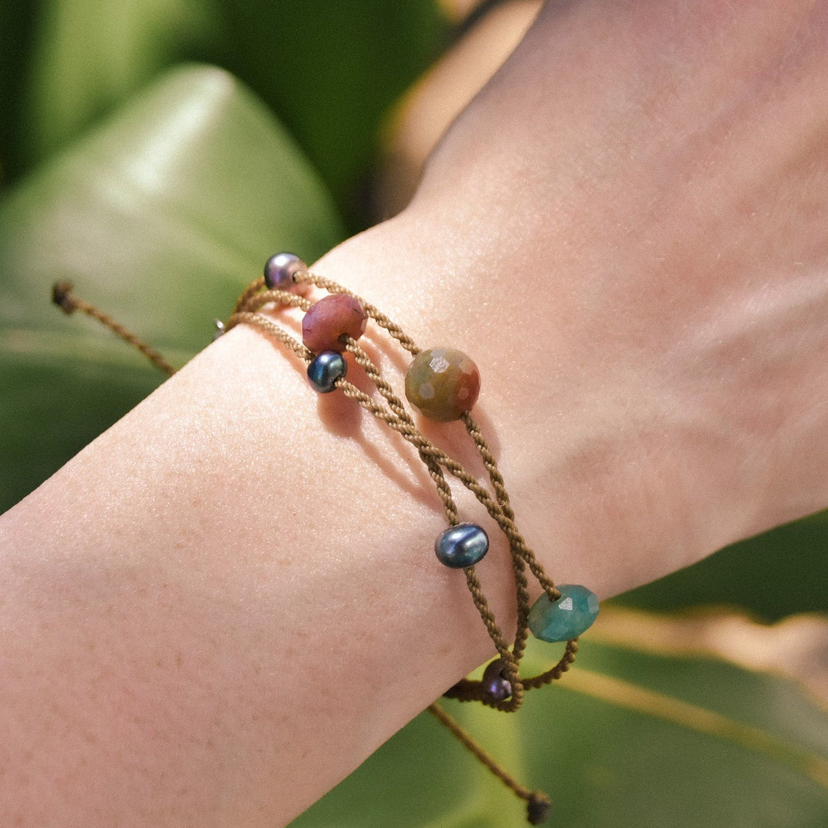 waterproof rope bracelet with india agate stones and peacock pearls on a wrist in from of greenery