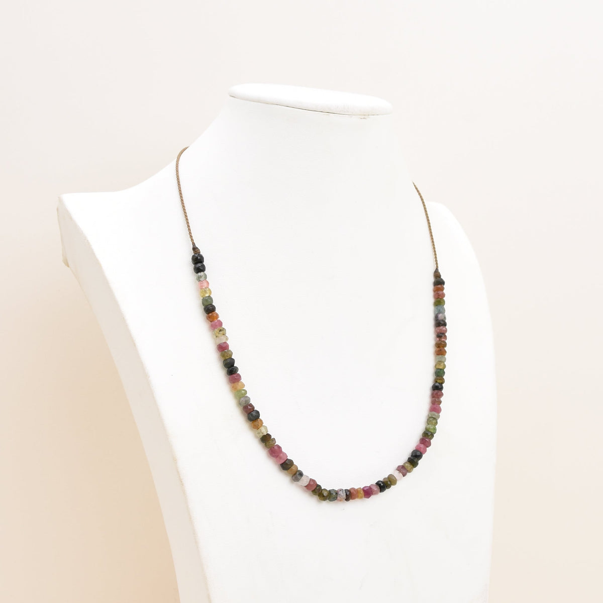 A watermelon tourmaline necklace displayed on a white mannequin bust against a plain off-white background.