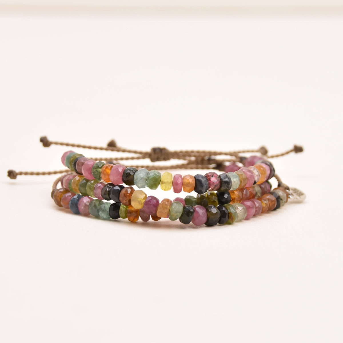 A close-up of a multi-strand beaded bracelet with adjustable rope ends, featuring small multicolored watermelon tourmaline gemstone rondelles on a plain white background.