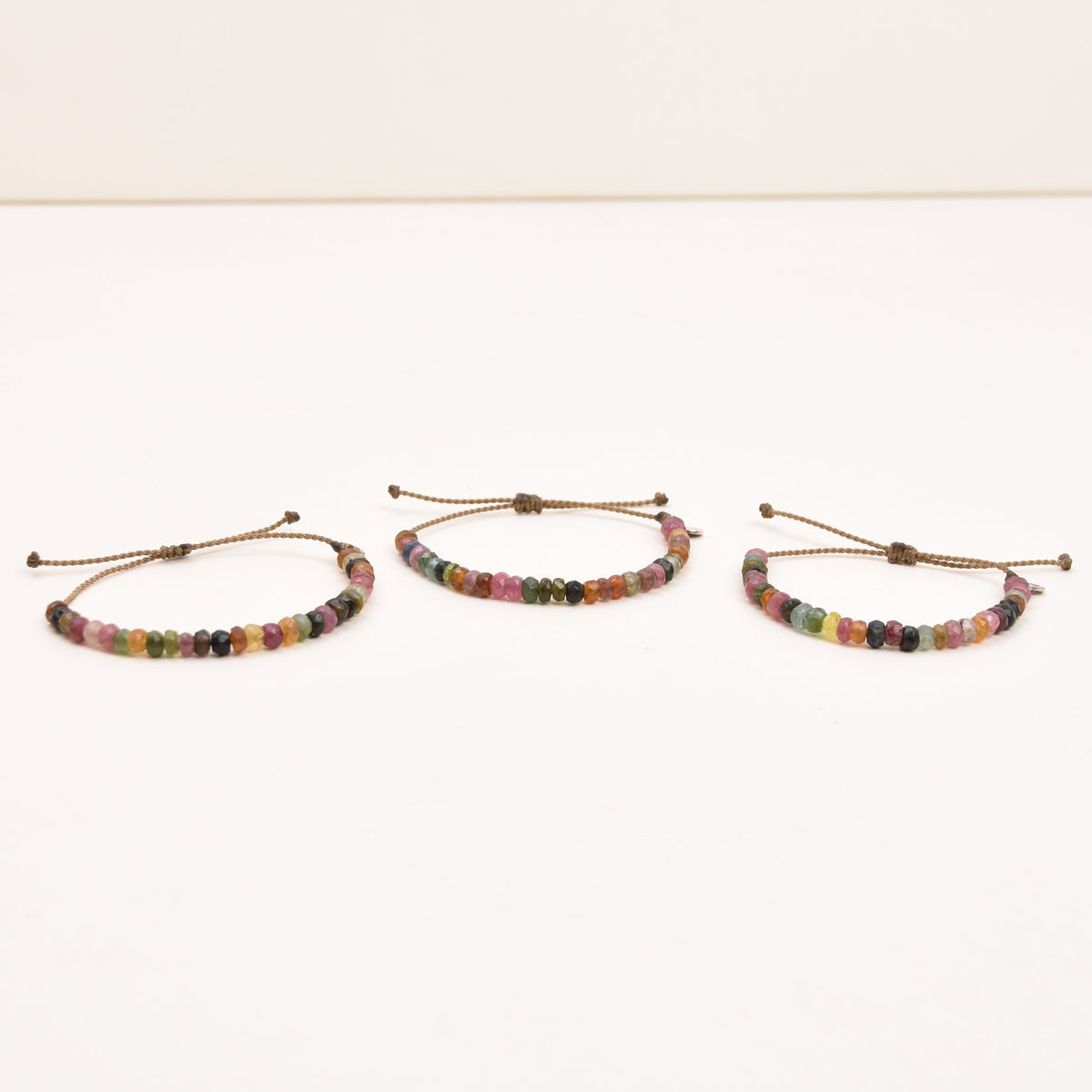 Three adjustable rope bracelets with multicolor watermelon tourmaline beads, arranged on a plain white surface.